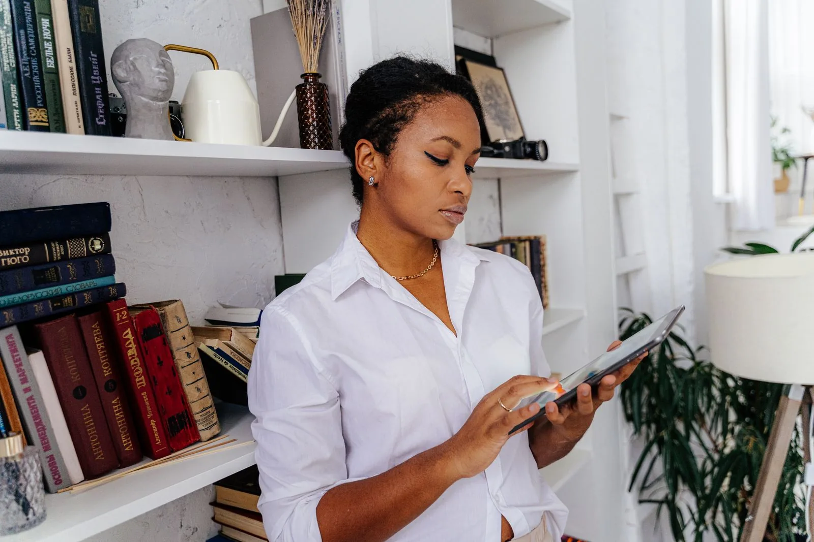 A person reviewing content on a tablet in front of a bookshelf